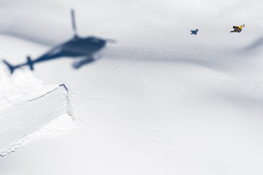 Snowboarder Austen Sweetin being chased off a jump by the shadow of a helicopter